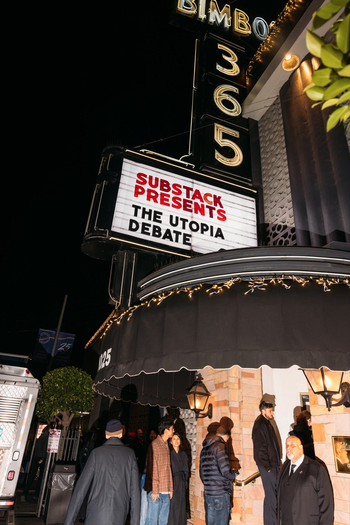 A theater marquee reads “SUBSTACK PRESENTS THE UTOPIA DEBATE” with people gathered under string lights outside the entrance at night.